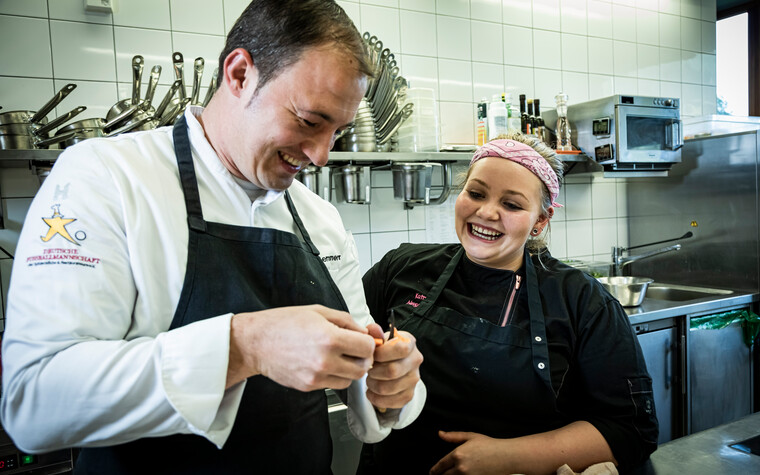 Katrin looks over chef Sascha's shoulder | © Kleinwalsertal Tourismus | Fotograf: Werner Krug