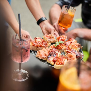 Menschen bei einem Sommer-Event im Kleinwalsertal, die Pizza servieren und Cocktails trinken. | © Kleinwalsertal Tourismus eGen • Fotograf: Oliver Farys