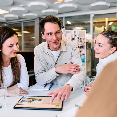 Vier Personen in einem Büro bei einem Meeting, ein Mann erklärt etwas, alle wirken interessiert. | © Kleinwalsertal Tourismus eGen • Fotograf: Oliver Farys