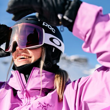 Junge Frau beim Skifahren im Winter, trägt pinke Skimode, Helm und Skibrille, lächelt | © Kleinwalsertal Tourismus eGen • Fotograf: Oliver Farys